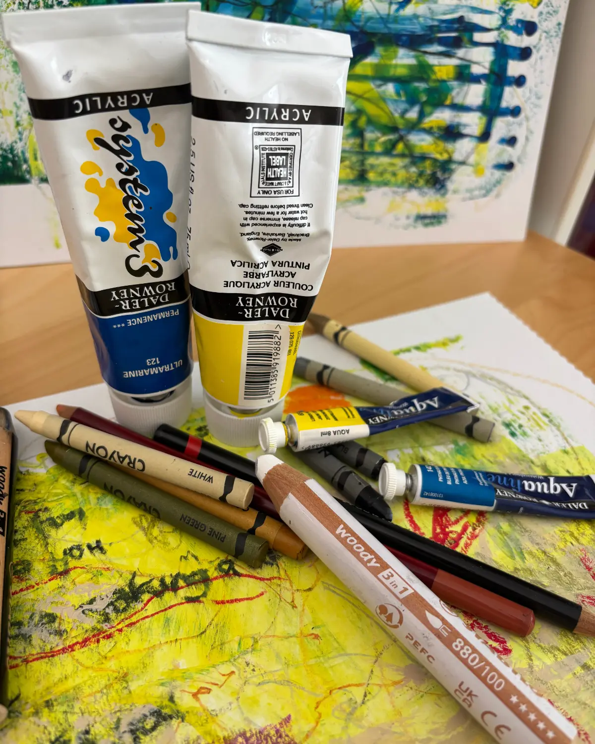 Mixed art materials including acrylic paint, crayons and pencils on a painted surface.